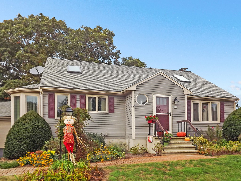 tan detached condo with reddish shutters, fall decorations on the front stairs and a scarecrow out front