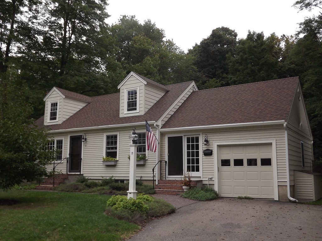 detached beige cape style home surrounded by trees, a cloudy sky